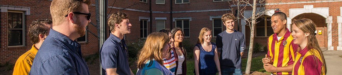 Photo of orientation leaders stopped in front of a residency hall while touring with students through campus